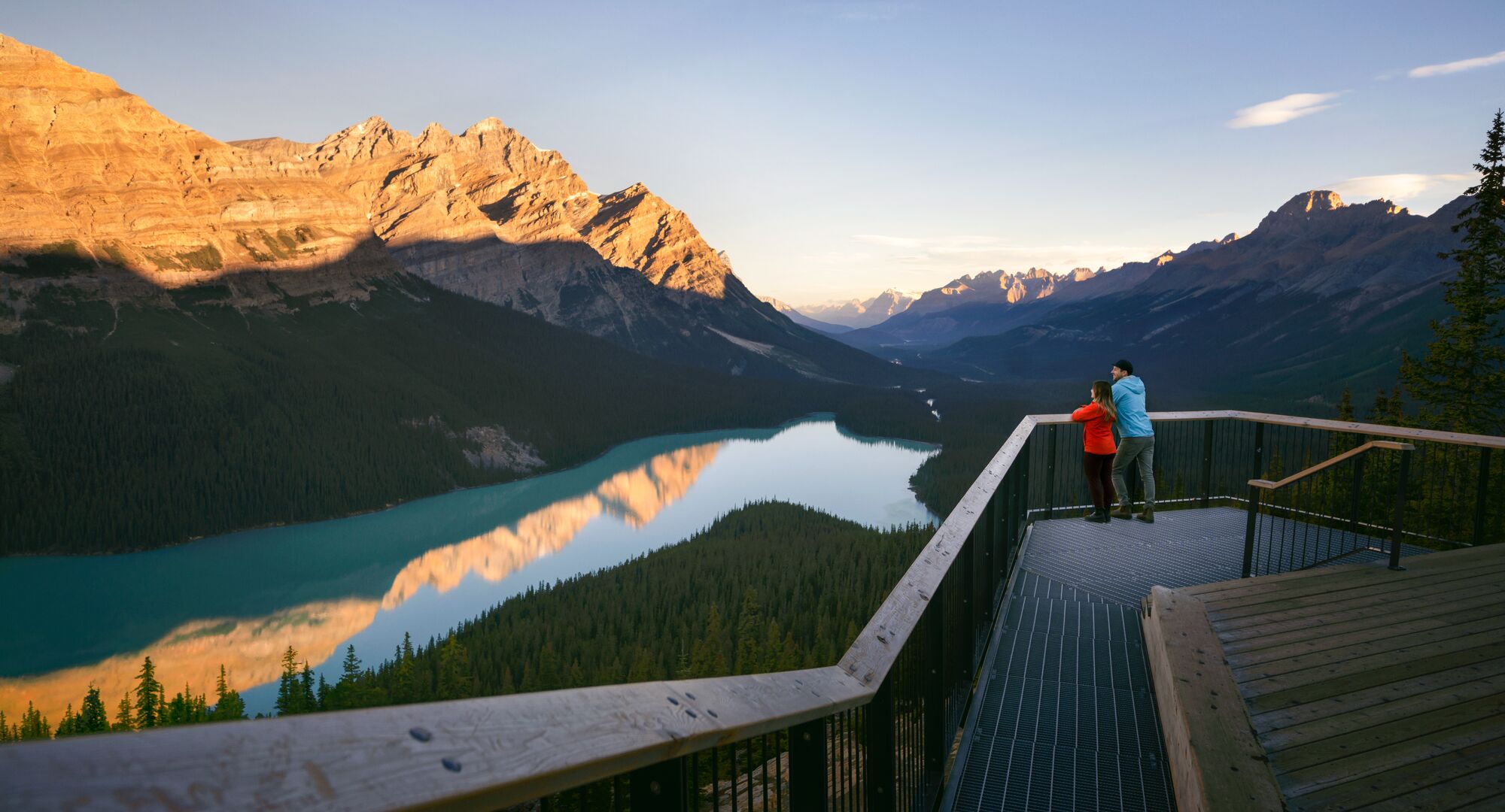 A couple stand on the viewing deck looking out at the view of Peyto Lake and the surrounding mountains.